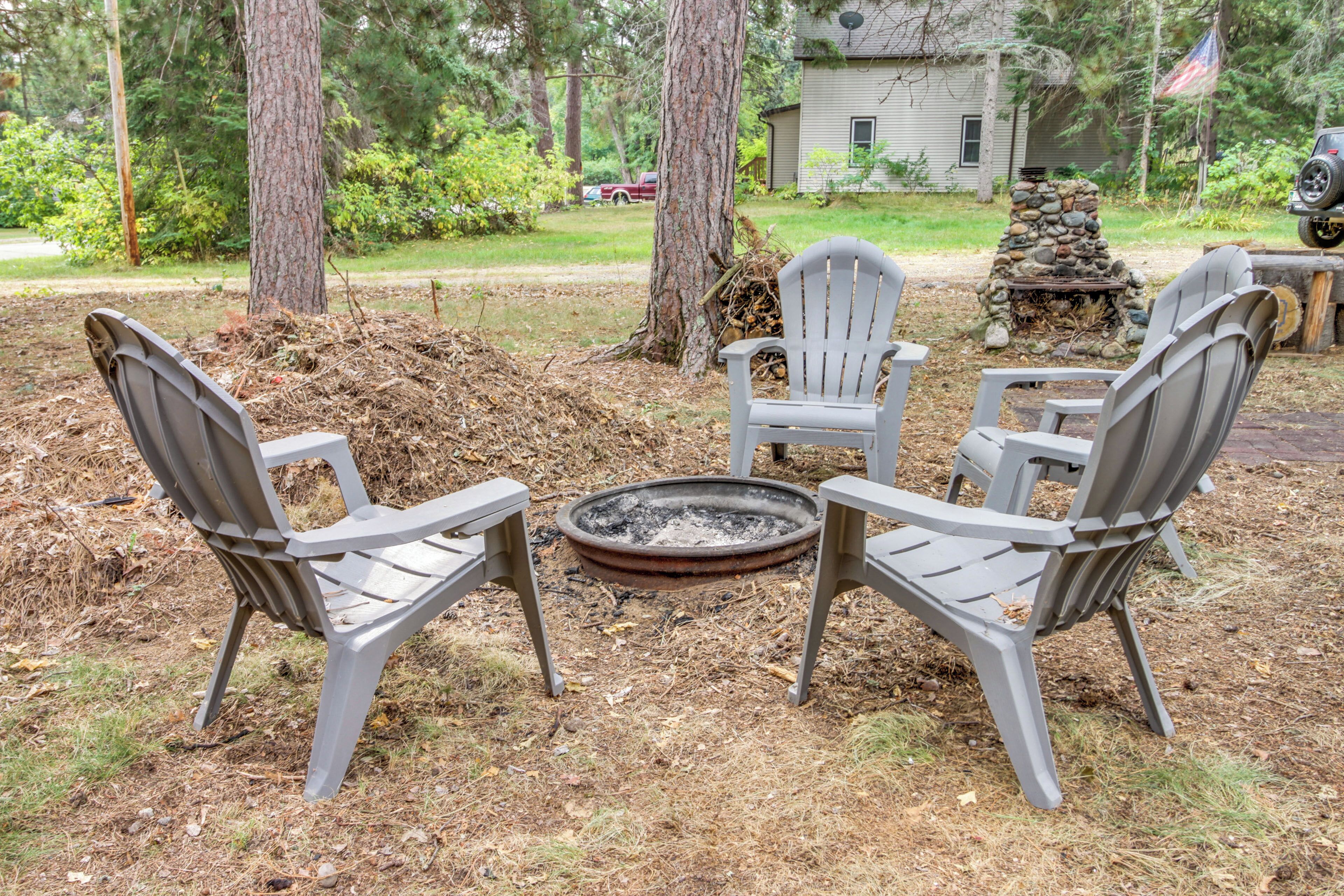 A backyard with a fire pit surrounded by Adirondack chairs.