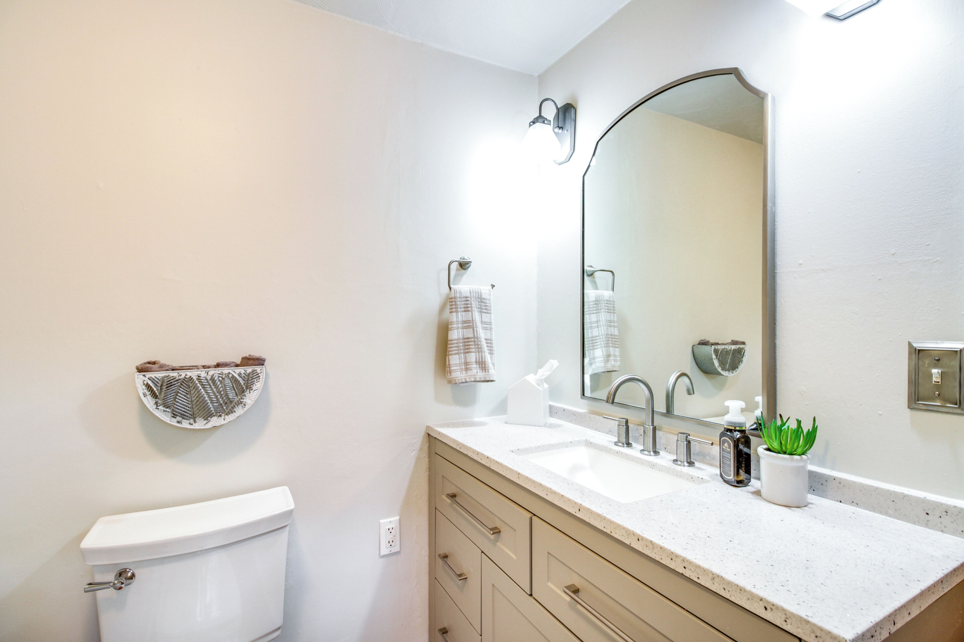A bathroom with a toilet, a sink, a mirror, a towel rack, and a soap dispenser.