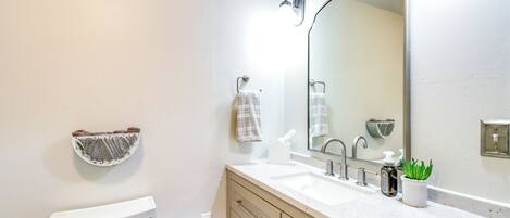 A bathroom with a toilet, a sink, a mirror, a towel rack, and a soap dispenser.