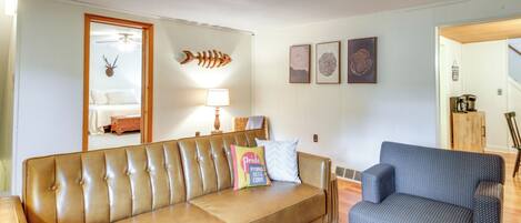 A living room with a brown leather sofa, a blue patterned armchair, a lamp, and wall art.