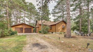 A two-story log cabin with a garage, surrounded by a forested area. - Pet-friendly Pequot Lakes Vacation Rental Cabin! (Pequot Lakes)