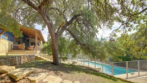 A stone pathway leading to a pool surrounded by a fence, with a large tree and a building with a porch in the background. - Pool & Covered Patios: Sprawling Austin Estate! (Austin)