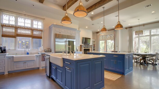 A modern kitchen with blue cabinets, a large island, pendant lighting, and a dining area with a table and chairs. - Pool & Covered Patios: Sprawling Austin Estate! (Austin)