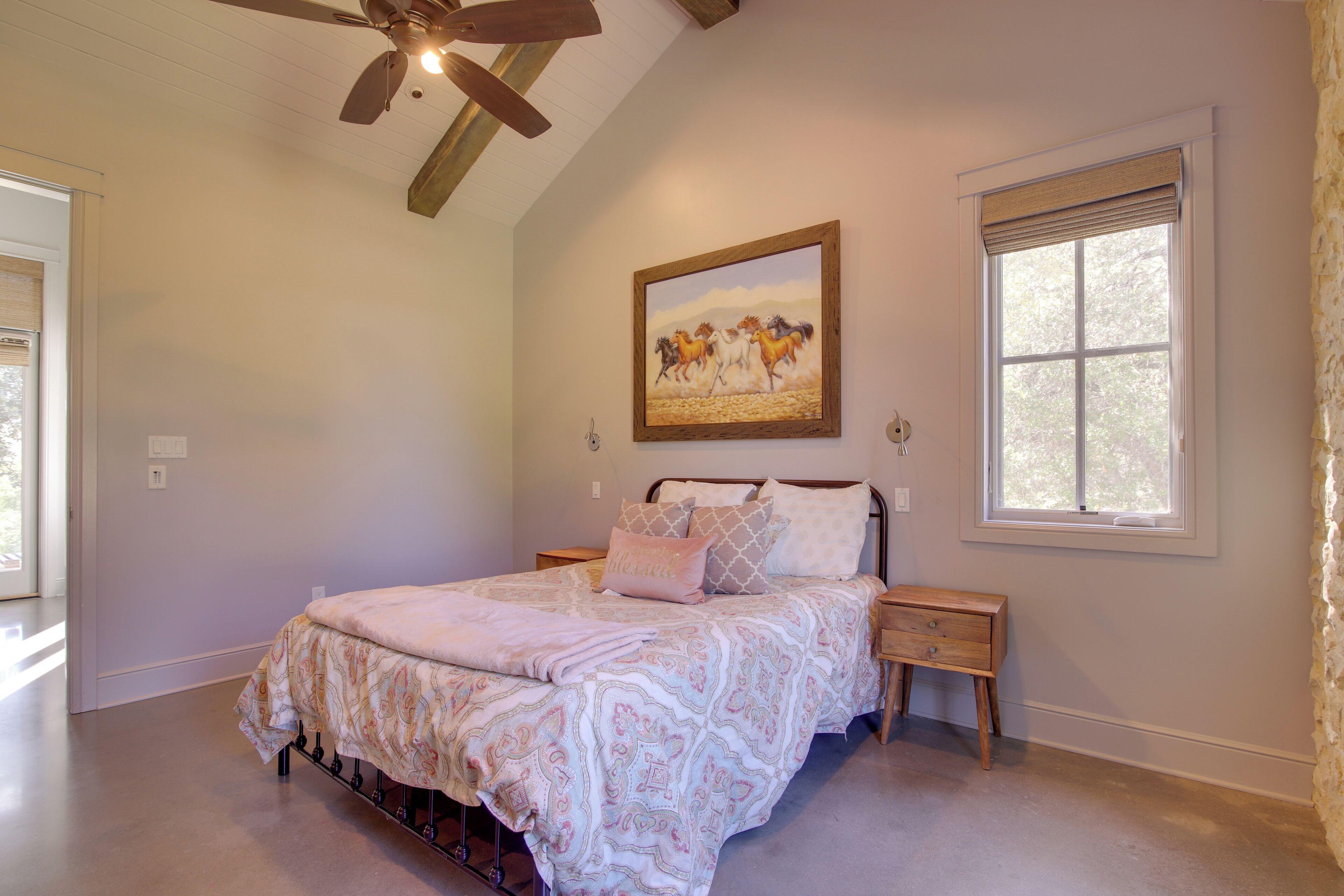 A bedroom with a bed, nightstands, a ceiling fan, a window with blinds, and a painting on the wall.