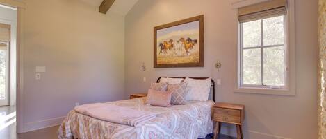 A bedroom with a bed, nightstands, a ceiling fan, a window with blinds, and a painting on the wall.