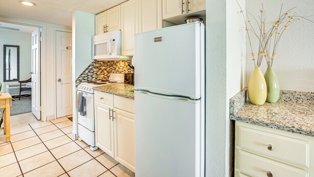 Una cocina con armarios blancos, microondas, refrigerador y salpicadero de azulejos.