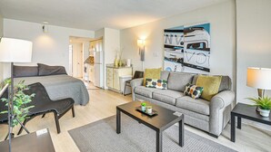 Una habitación moderna y luminosa con cama, sofá gris, mesa de centro y televisor.