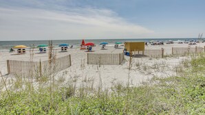 Una playa con sombrillas, sillas y una valla de madera.