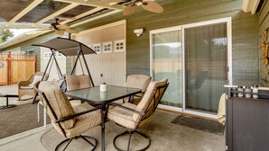 Un patio techado con una mesa, sillas, ventilador de techo y puerta corredera de vidrio.