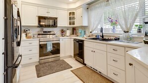 Una cocina moderna con armarios blancos, electrodomésticos de acero inoxidable y una ventana con cortinas ligeras.