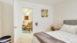 Un dormitorio con cama, una puerta que da a otra habitación, una obra de arte en la pared y una mesita de noche con lámpara.
