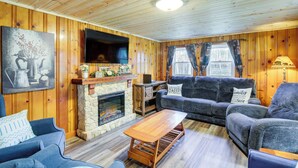 A cozy living room with wooden walls, a stone fireplace, a flat-screen TV, and comfortable seating. - Fire Pit & Covered Deck! Cozy, Rustic Cosby Cabin (Cosby)