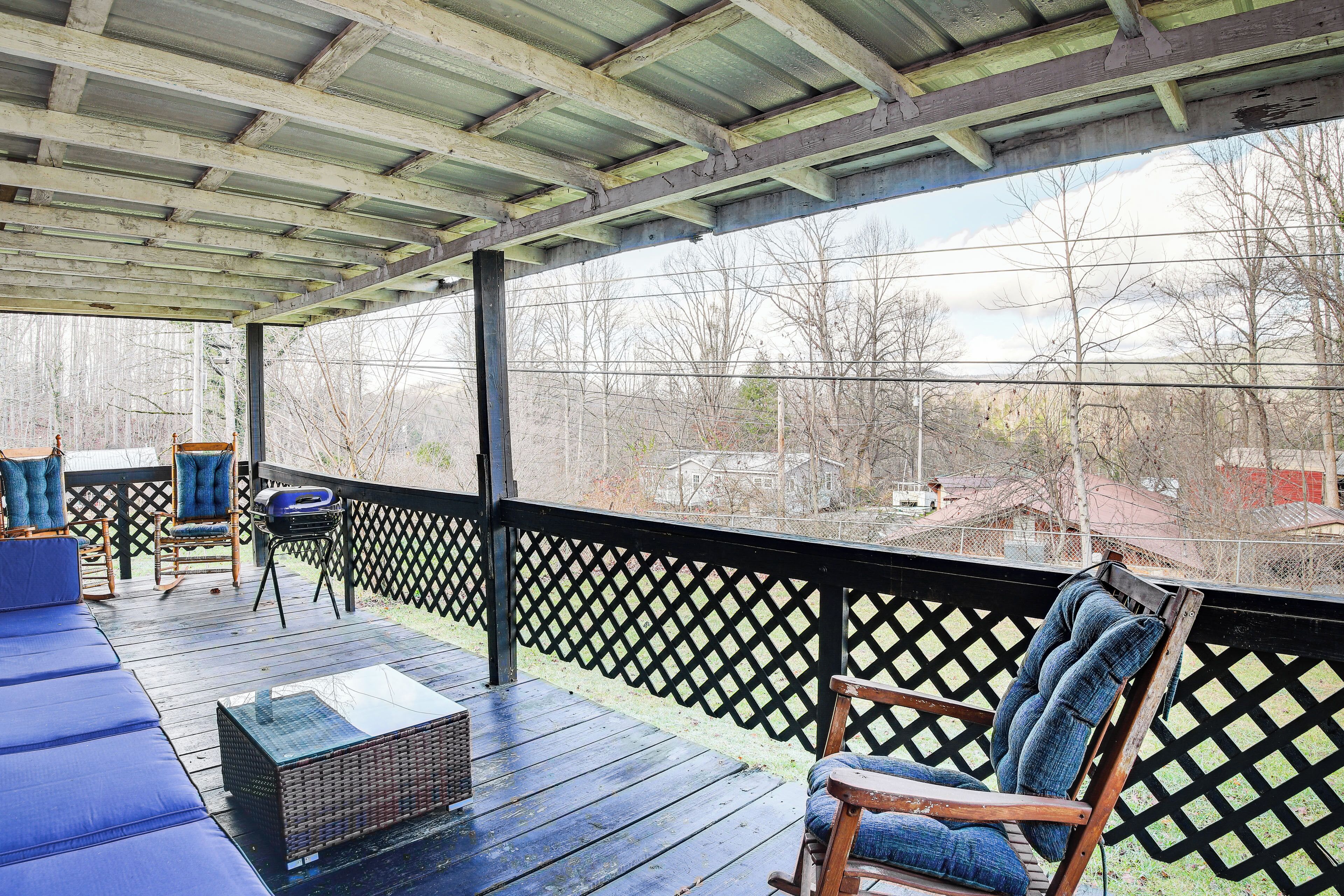 A covered outdoor deck with a wooden floor, blue cushioned seating, and a wooden rocking chair.