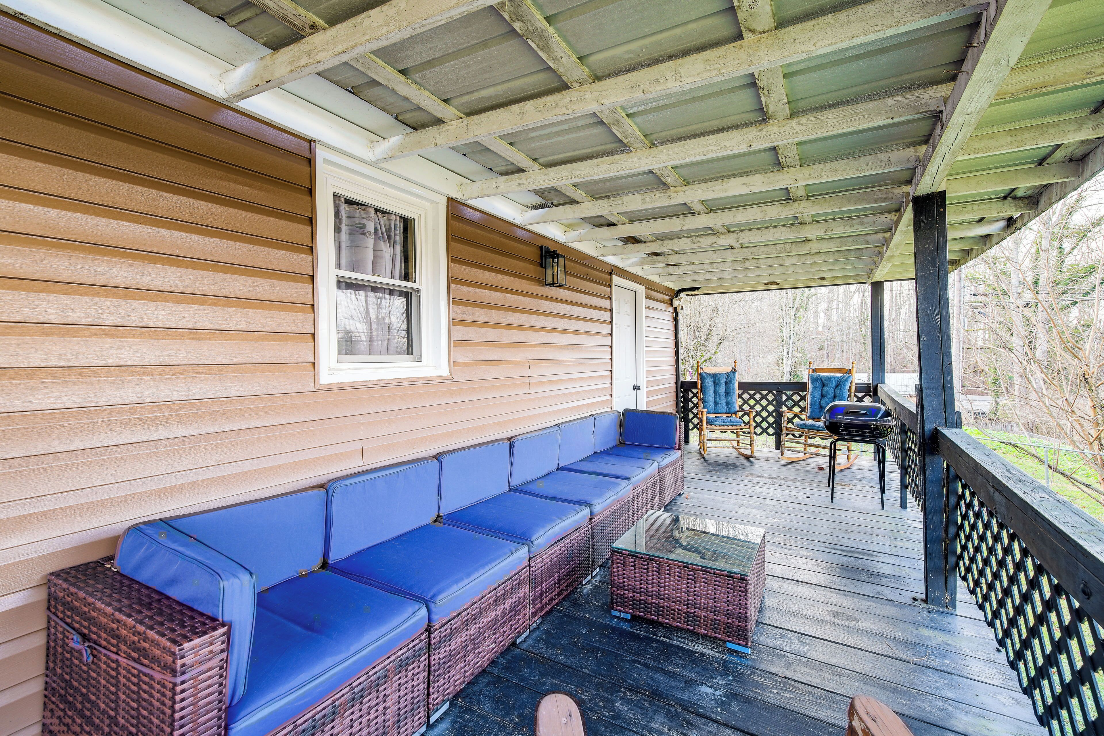 A covered porch with a blue cushioned bench, wicker furniture, and a view of trees.