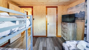 A room with a bunk bed, a television, a dresser, and a door leading to another room. - Fire Pit & Covered Deck! Cozy, Rustic Cosby Cabin (Cosby)