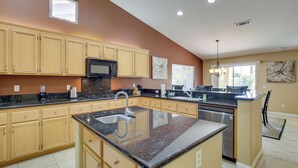A modern kitchen with beige cabinets, granite countertops, a stainless steel dishwasher, and a large island with a sink. - Resort Perks, Patio & Gas Grill: Indio Retreat! (Indio)