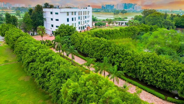 A multi-story building surrounded by lush greenery, with a well-maintained garden and a clear view of the surrounding landscape. - HITE Resort Greater Noida (Greater Noida)