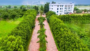 A pathway flanked by lush greenery and a white building with multiple floors. - HITE Resort Greater Noida (Greater Noida)