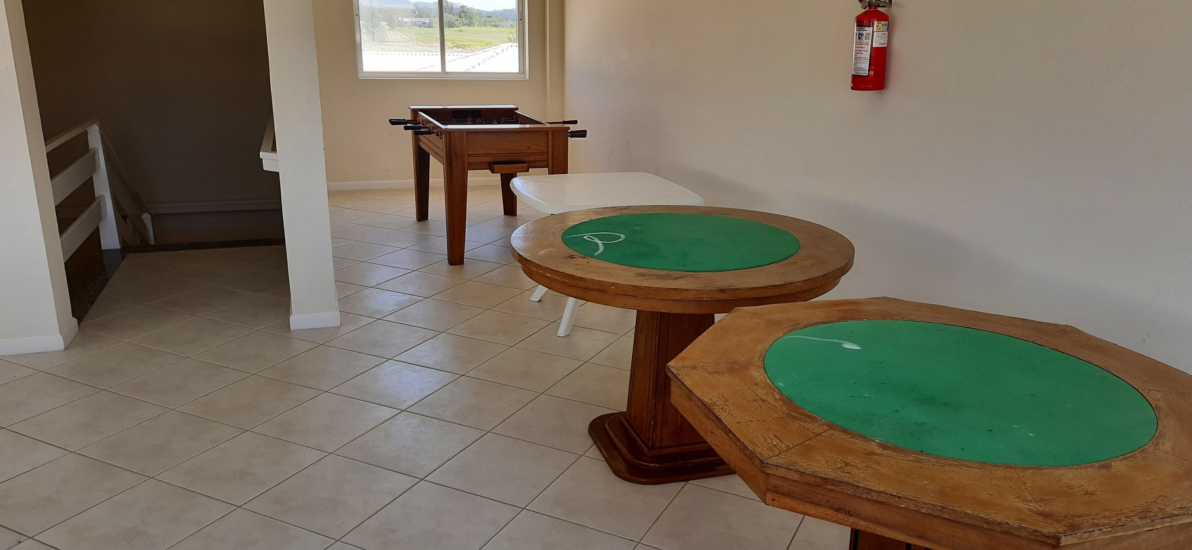 A room with a foosball table, a white table, and a fire extinguisher on the wall.