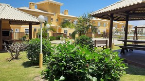 Une cour avec des espaces de détente en plein air, un coin barbecue et une piscine en arrière-plan.