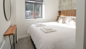 A bedroom with a bed, a window, a bedside table, and a painting on the wall. - Watch Tree Apartment (Ulverston)