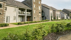 A row of modern multi-story residential buildings with balconies, stone facades, and a well-maintained lawn. - Watch Tree Apartment (Ulverston)