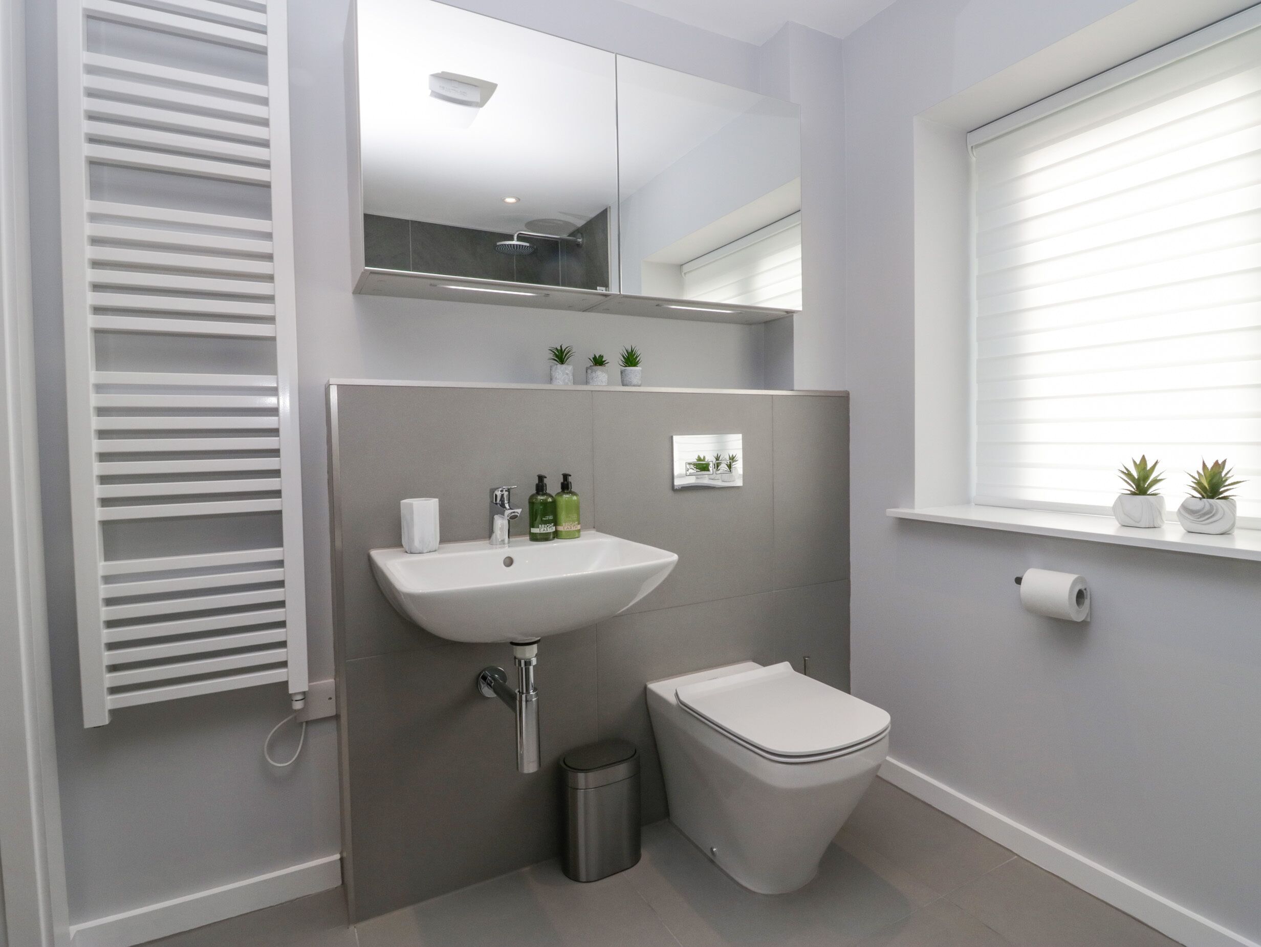 A modern bathroom with a white sink, toilet, and a window with blinds.