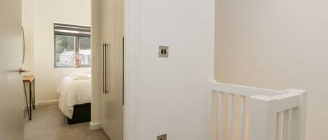 A hallway with a bed, a desk, and a white door with a light switch.