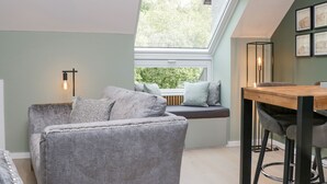 A cozy room with a grey sofa, a wooden table, and a window with a view of greenery. - Watch Tree Apartment (Ulverston)