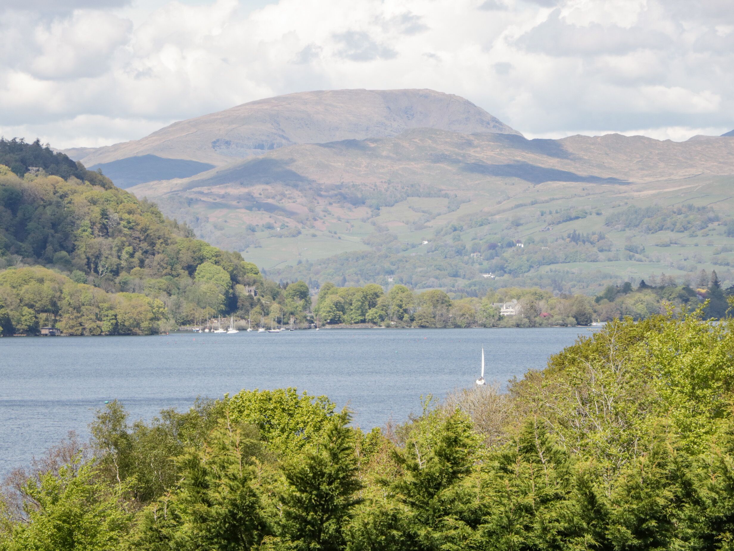 A lake surrounded by hills with a sailboat in the foreground.