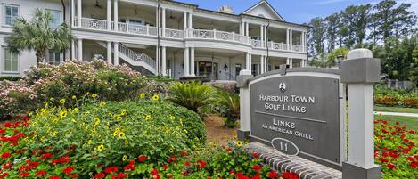 A large, two-story building with multiple balconies and a well-maintained garden with red and yellow flowers.