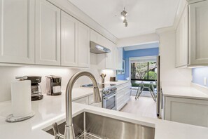 Une cuisine moderne avec des meubles blancs, des appareils en acier inoxydable et une vue sur l’extérieur.