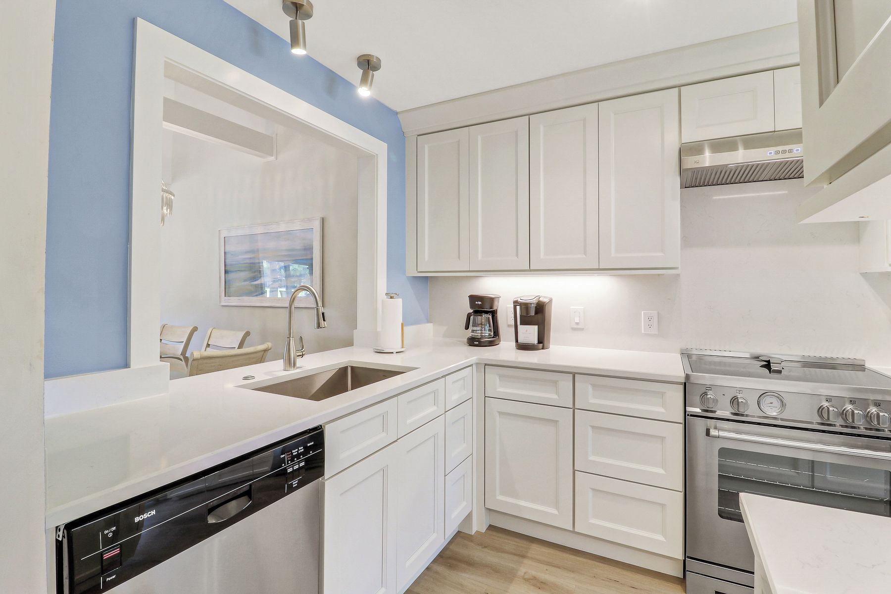 A modern kitchen with white cabinetry, a Bosch dishwasher, a coffee maker, and a stainless steel stove.