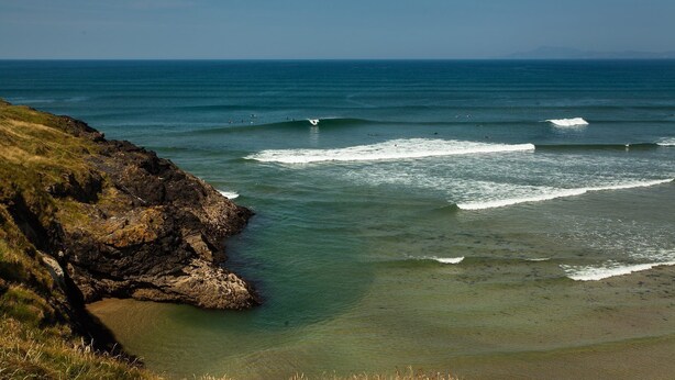 Paisagem costeira com águas azuis cristalinas, falésias rochosas e uma praia de areia.