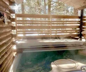 Ein Whirlpool in einer Blockhütte mit Holzgeländer und Blick auf Bäume.