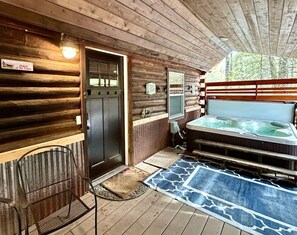 Una cabaña con fachada de madera, un jacuzzi, una puerta y una silla.