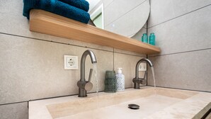 A bathroom with two sinks, a wooden shelf above the sinks, and a mirror above the shelf.