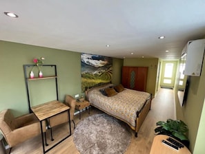 Ein Schlafzimmer mit Bett, Schreibtisch, Stuhl, einem kleinen Tisch, Teppich und einem Bild an der Wand.
