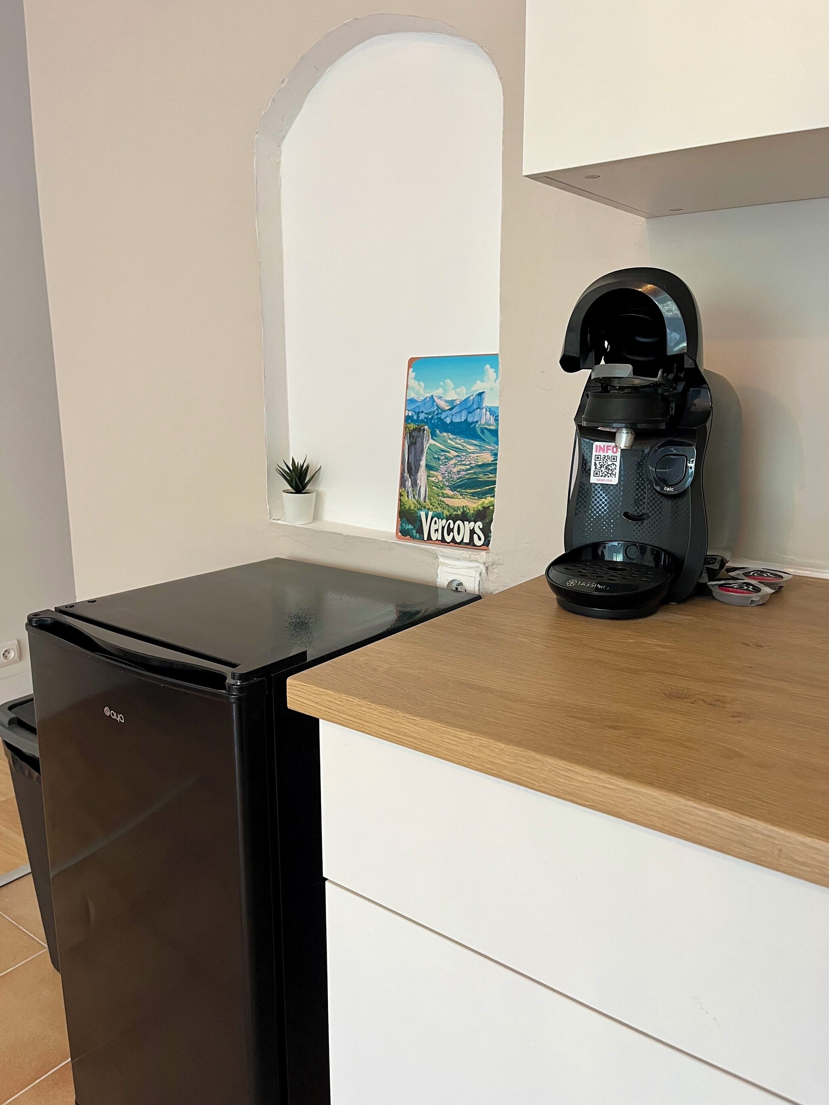 Una cocina compacta con un refrigerador negro, una cafetera y una pequeña planta en maceta.