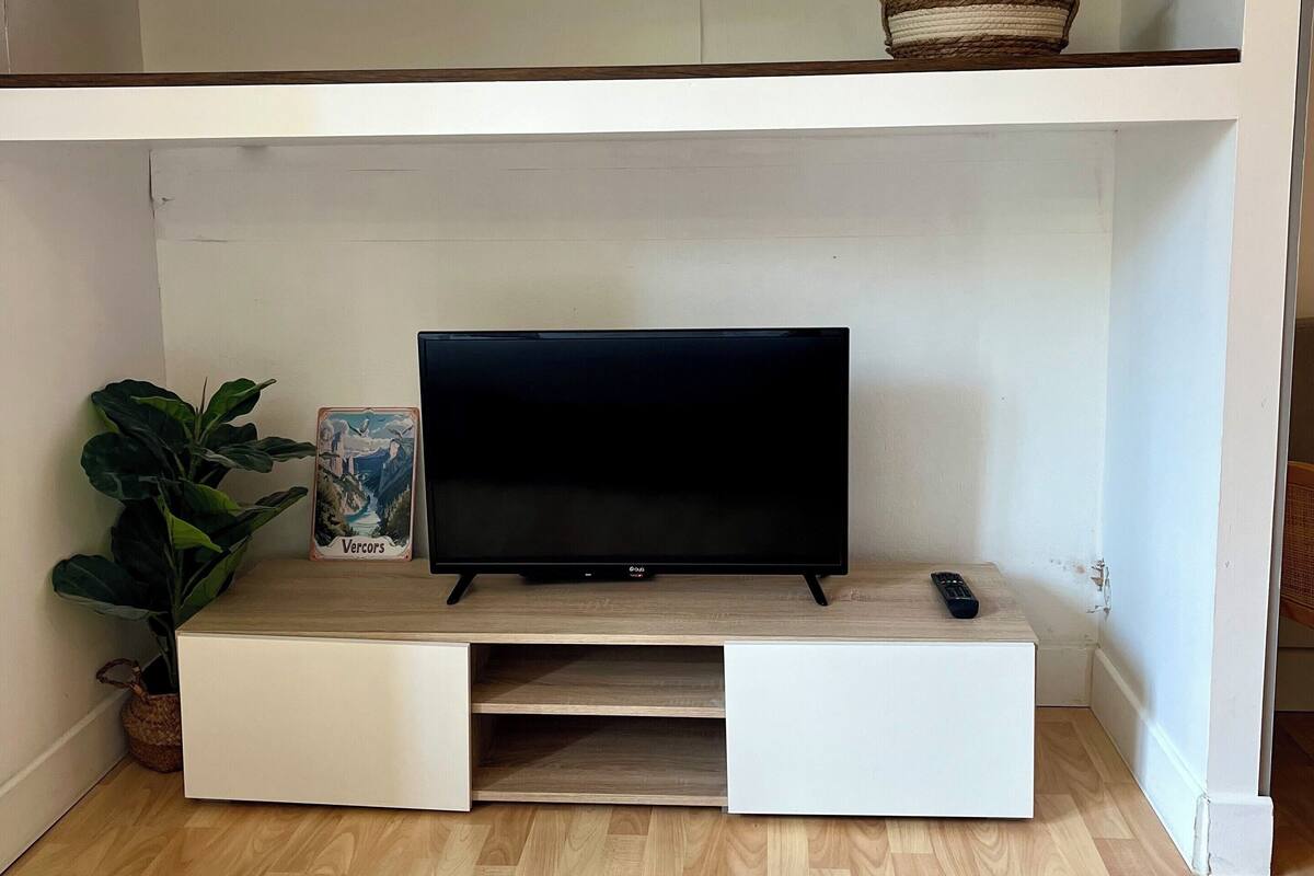 TV-taso on tehty puusta, ja sen päällä on kaukosäädin, kasvi ja kehystetty kuva alemmalla hyllyllä.