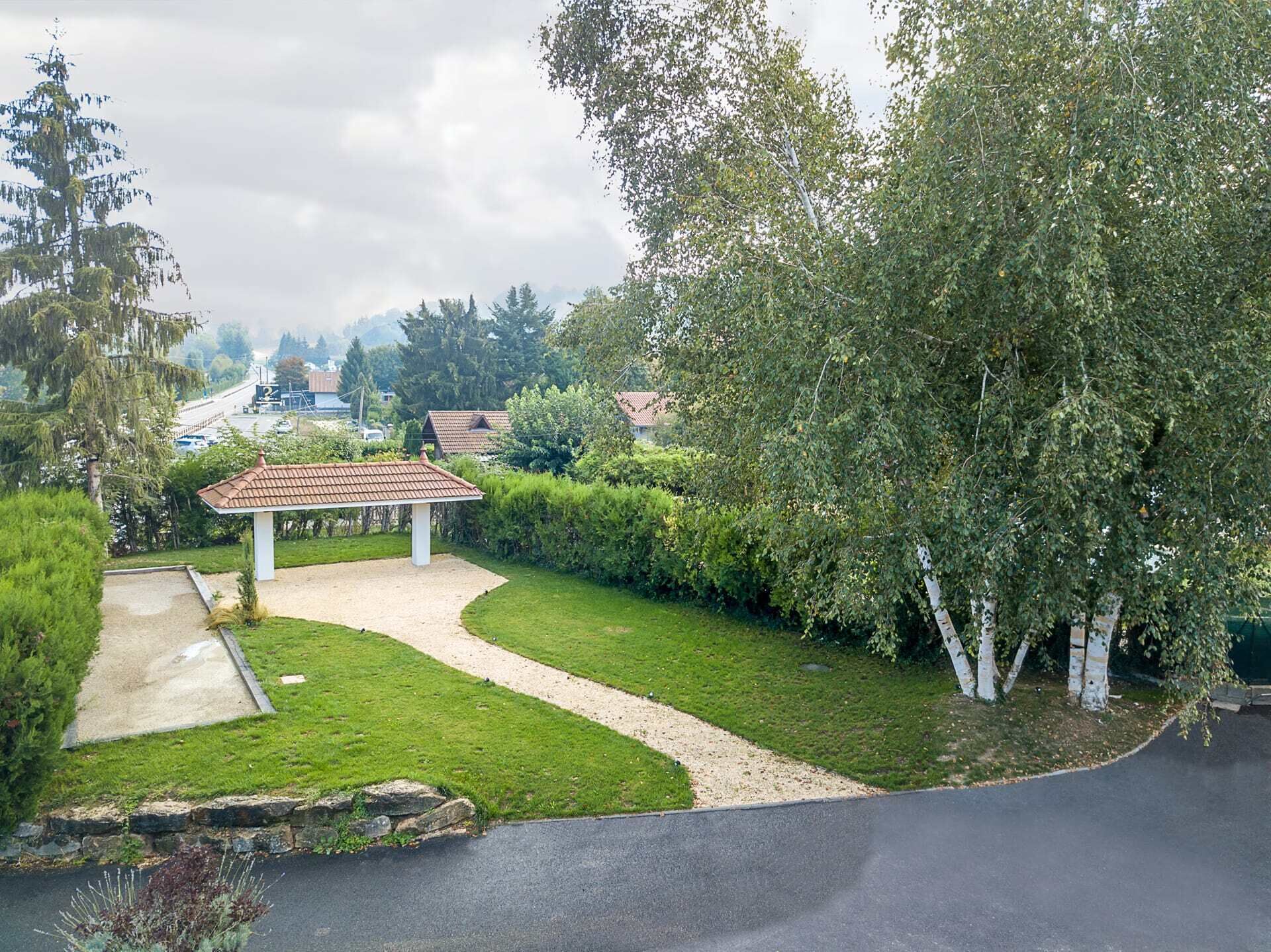 Un giardino curato con un gazebo, un vialetto ghiaioso e diverse piante e arbusti.