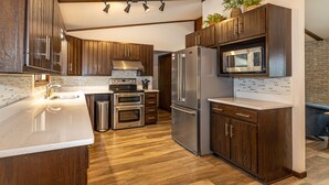A modern kitchen with wooden cabinets, stainless steel appliances, a built-in microwave, and a large island with a sink. - Minocqua Chain - SUMMER DATES AVAILABLE! (Minocqua)