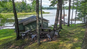 A lakeside cabin with a dock, surrounded by trees and a grassy area with outdoor seating. - Minocqua Chain - SUMMER DATES AVAILABLE! (Minocqua)