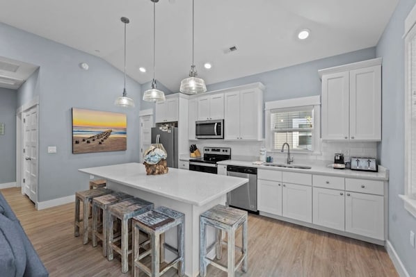Una cocina moderna con armarios blancos, una isla central con taburetes, microondas y un lavamanos.