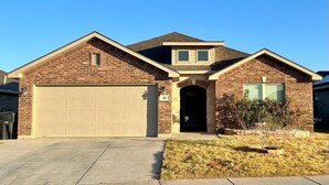 Une maison à deux étages, construite en briques, avec un garage, un petit porche et une pelouse bien entretenue.