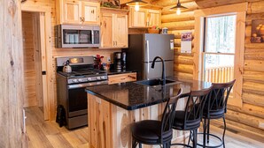 Une cuisine rustique aménagée dans une cabane en rondins, avec des meubles en bois, un réfrigérateur en acier inoxydable, un four à micro-ondes, une cuisinière et un évier.