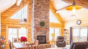 L’intérieur d’une cabane en rondins, avec une cheminée en pierre, une table à manger en bois et des sièges en cuir.
