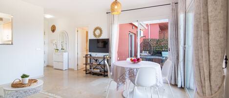 Una sala de estar luminosa con comedor, televisor y vistas al exterior.