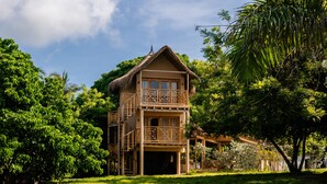 A two-story wooden house with a balcony, surrounded by lush greenery and a clear sky. - Anaho Beach Club (Cartagena)