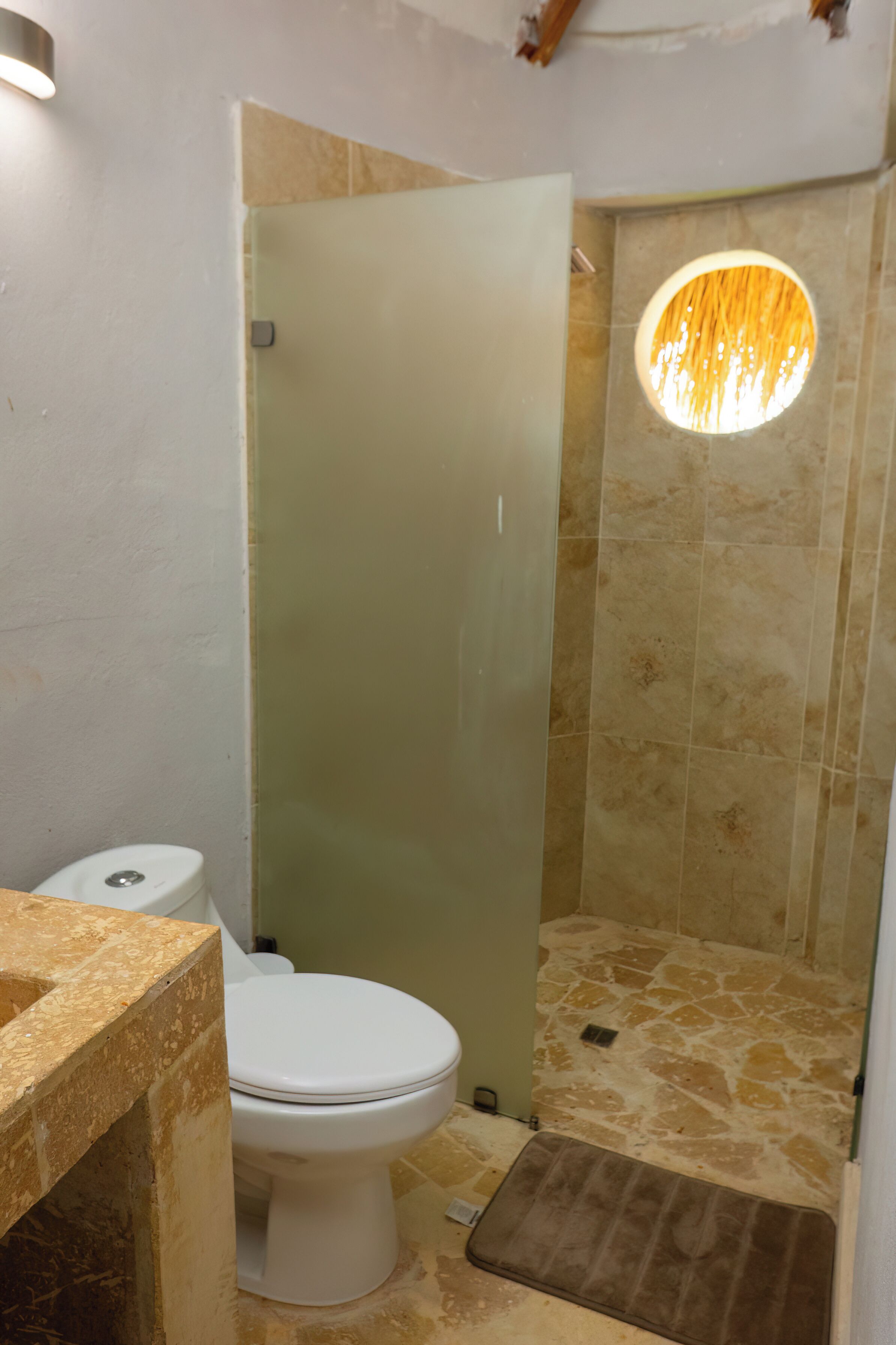 Un baño con inodoro, ducha con cerramiento de vidrio y una lámpara de techo circular.